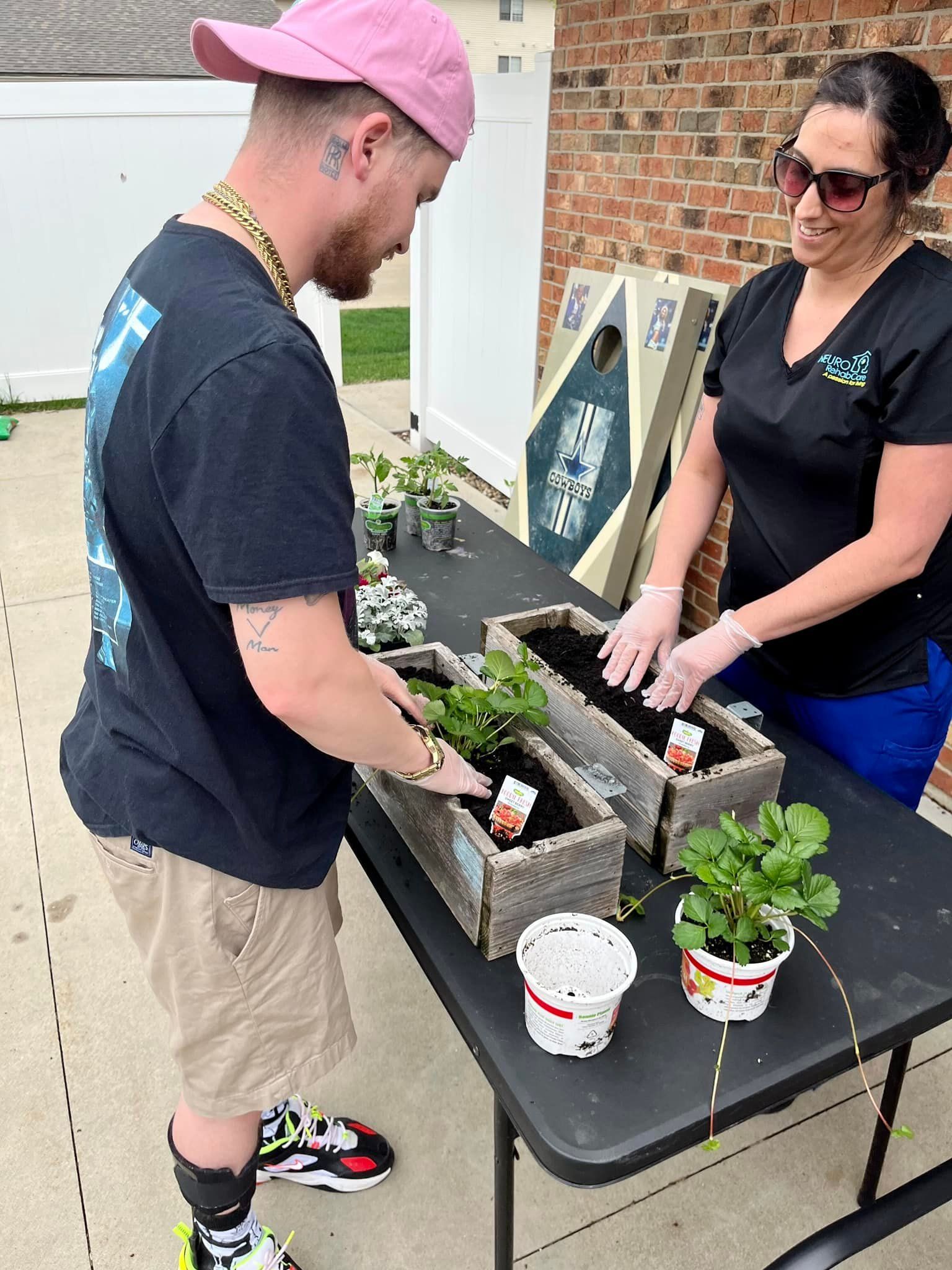 A man and a woman are planting plants in wooden planters on a table.