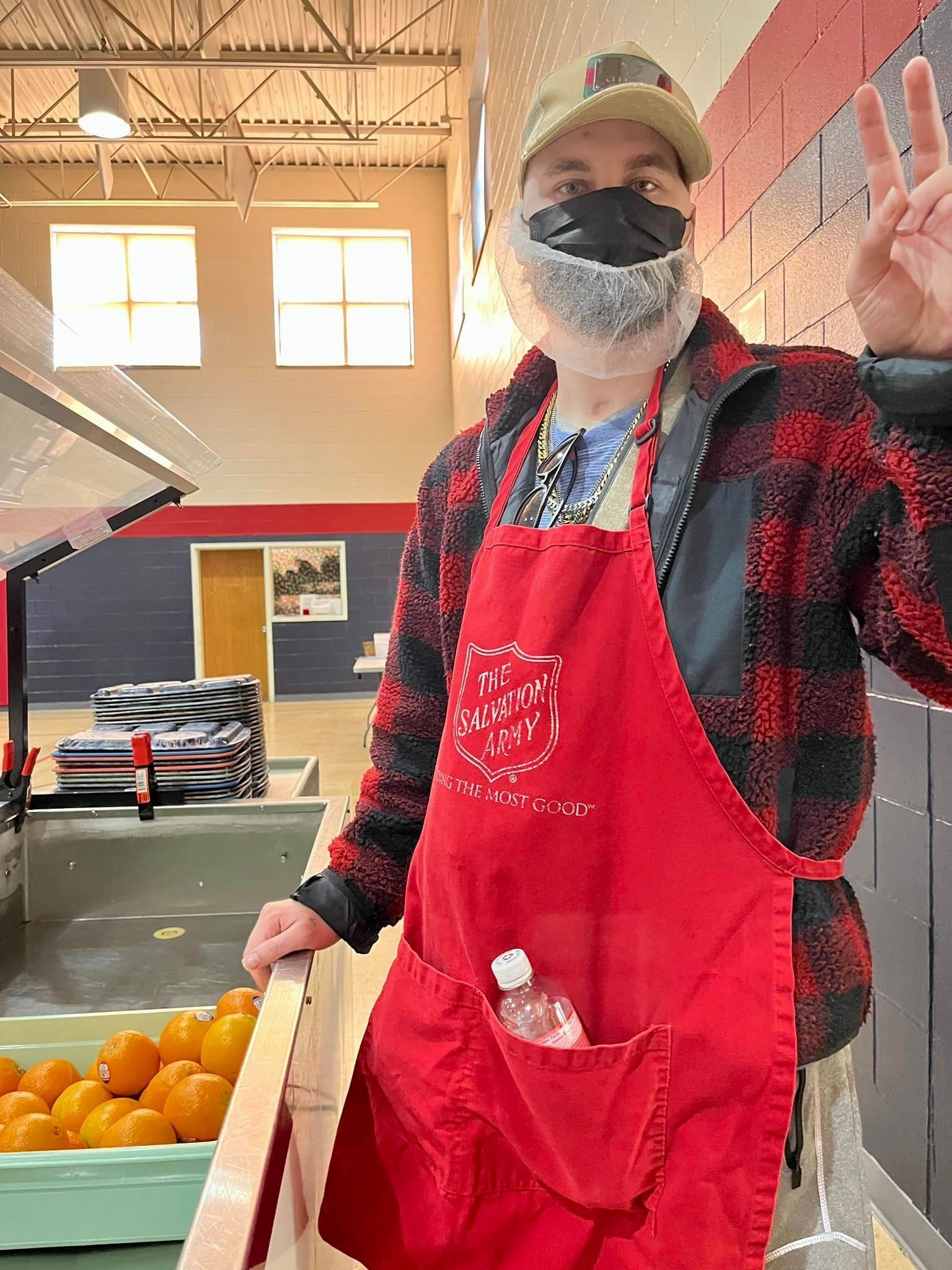 A man wearing a mask and an apron is giving a peace sign.