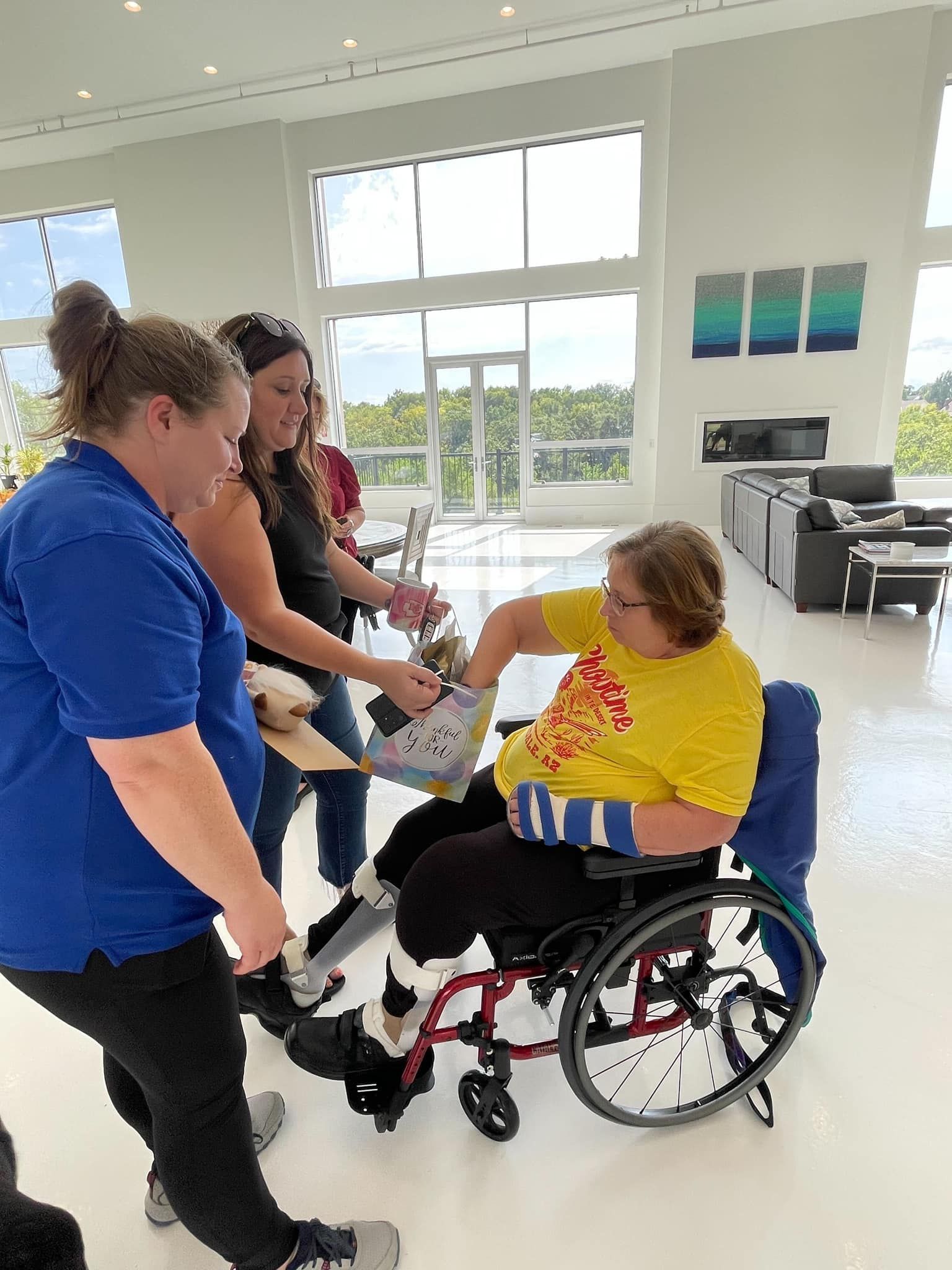 A woman in a wheelchair is being helped by two women.