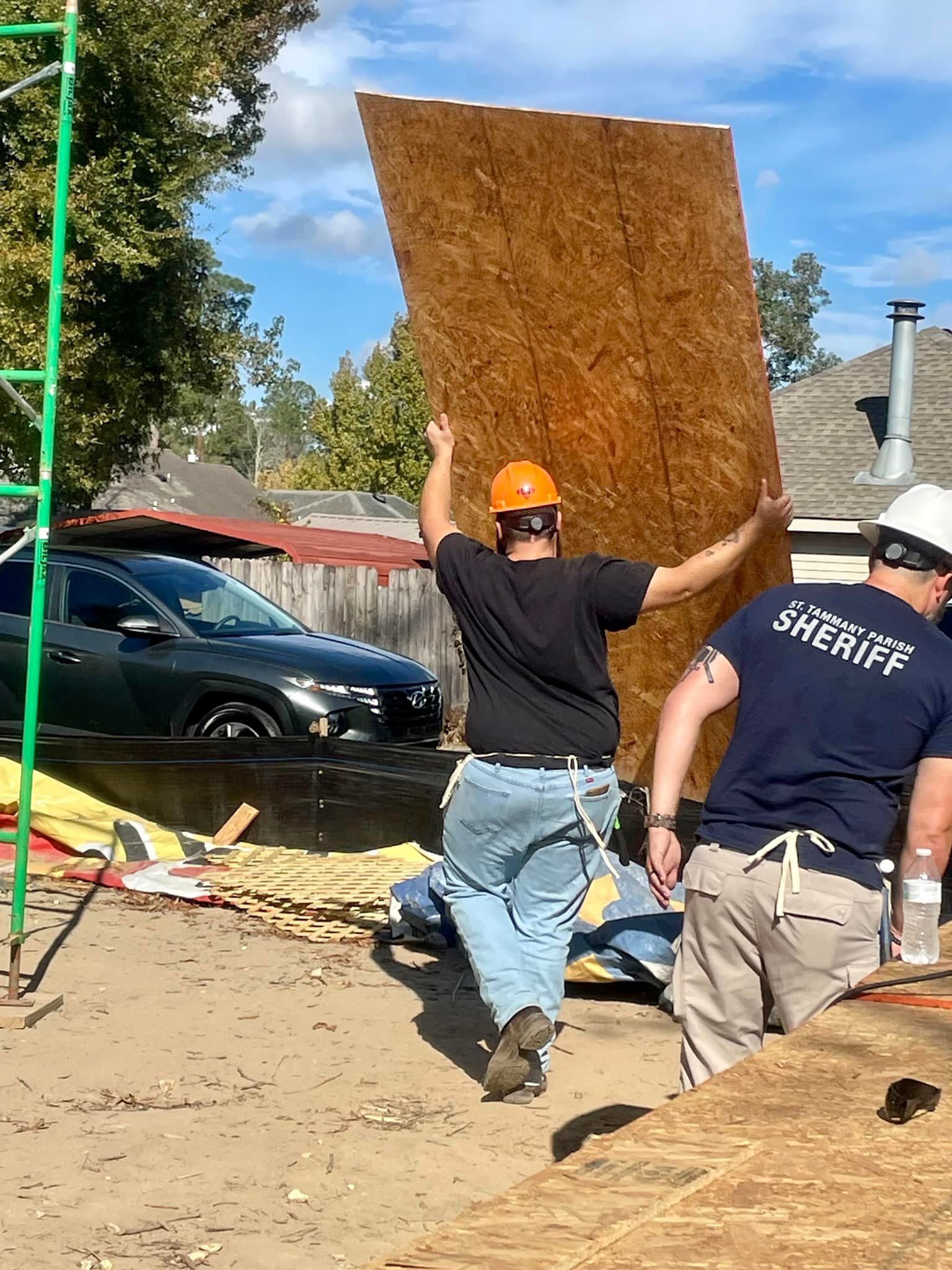 Two men are carrying a large piece of wood on a construction site.