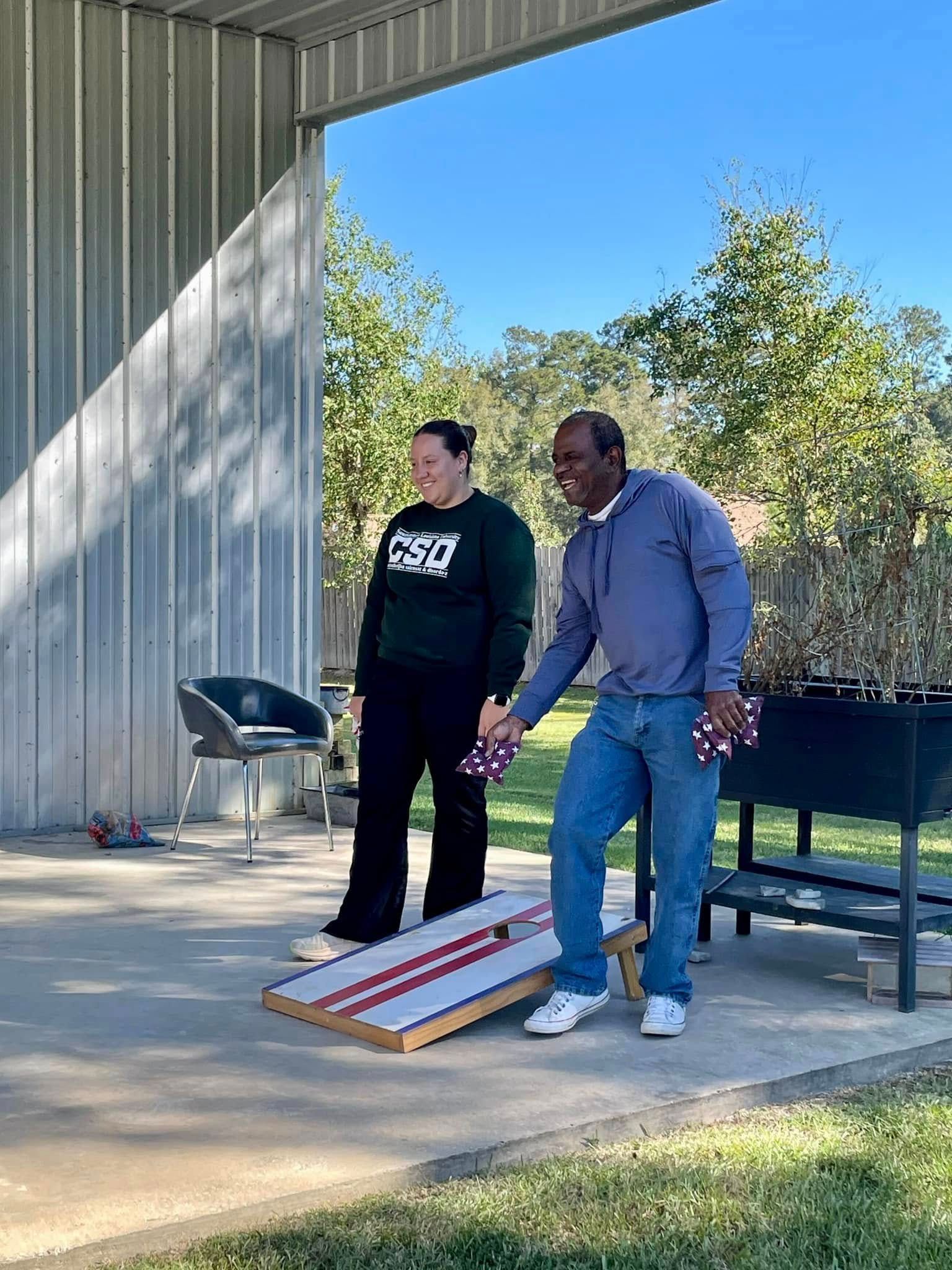 A man and a woman are playing a game of cornhole.