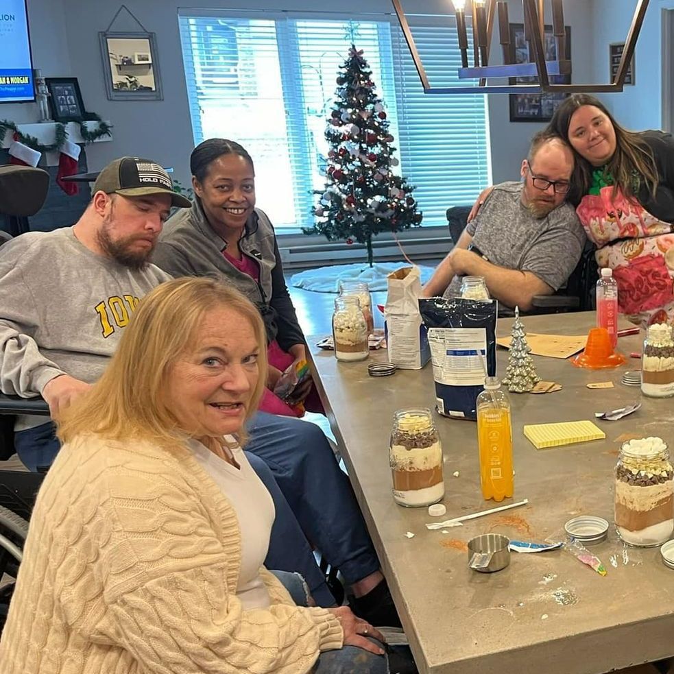A group of people are sitting around a table with a christmas tree in the background.