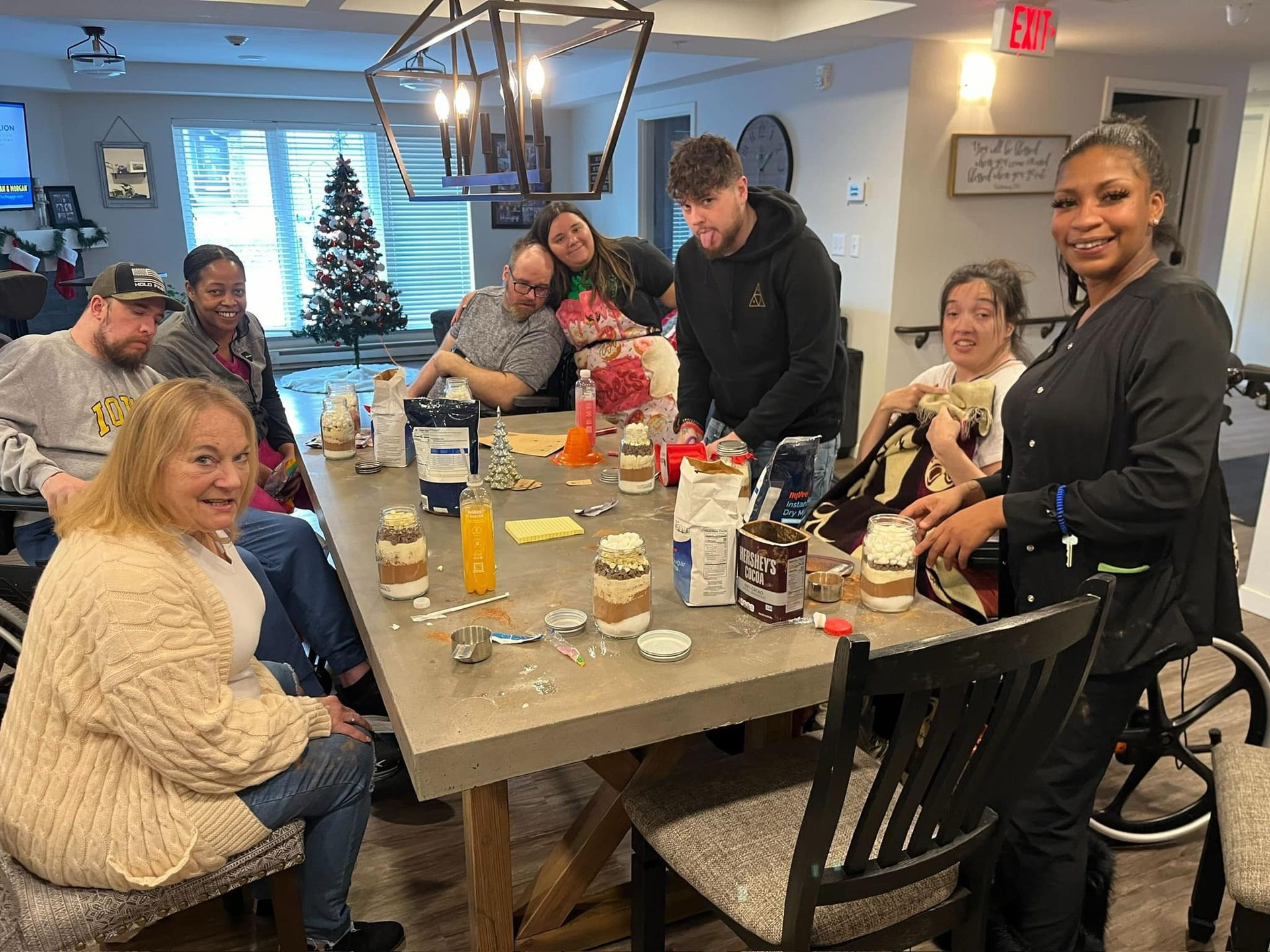 A group of people are sitting around a table with a christmas tree in the background.