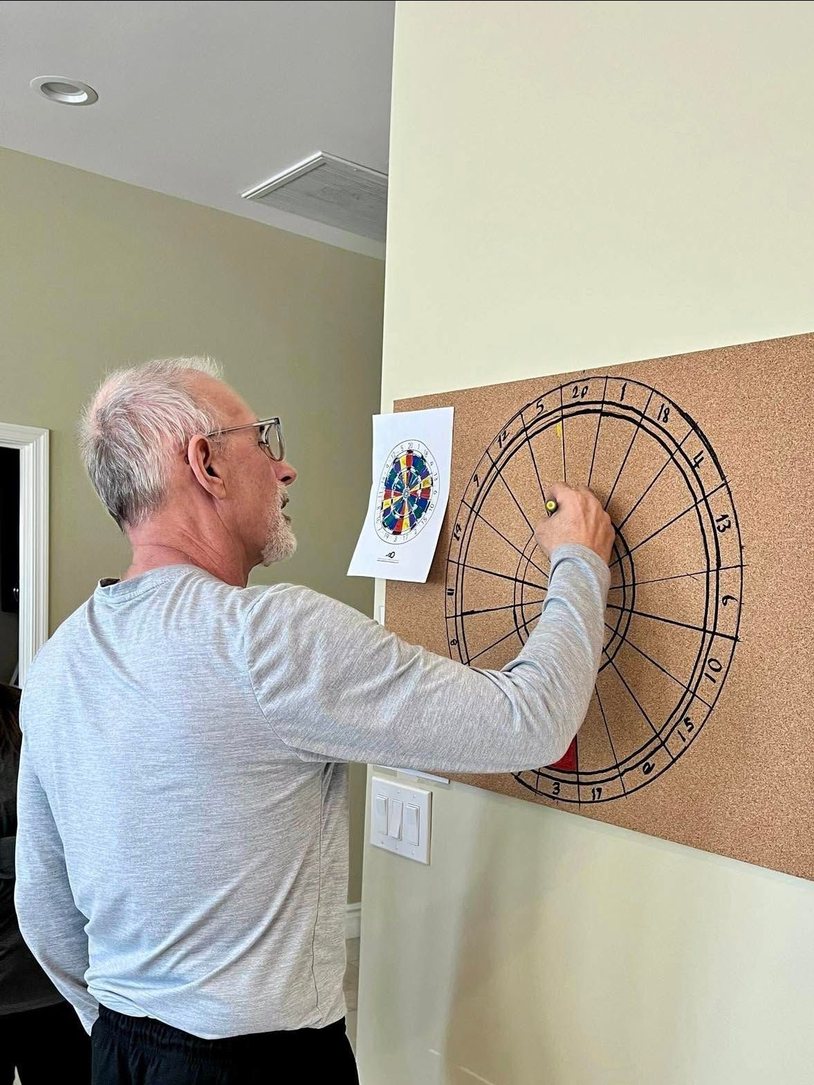 A man is standing in front of a dart board on a wall.
