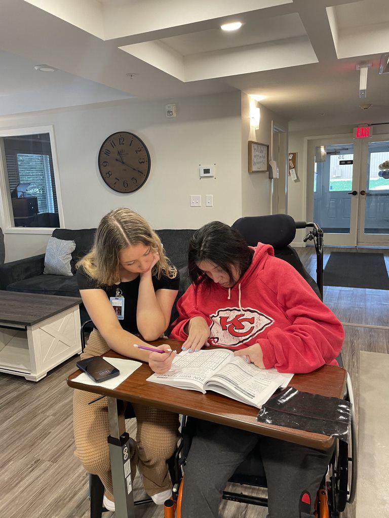 A woman in a wheelchair is sitting at a desk with another woman.