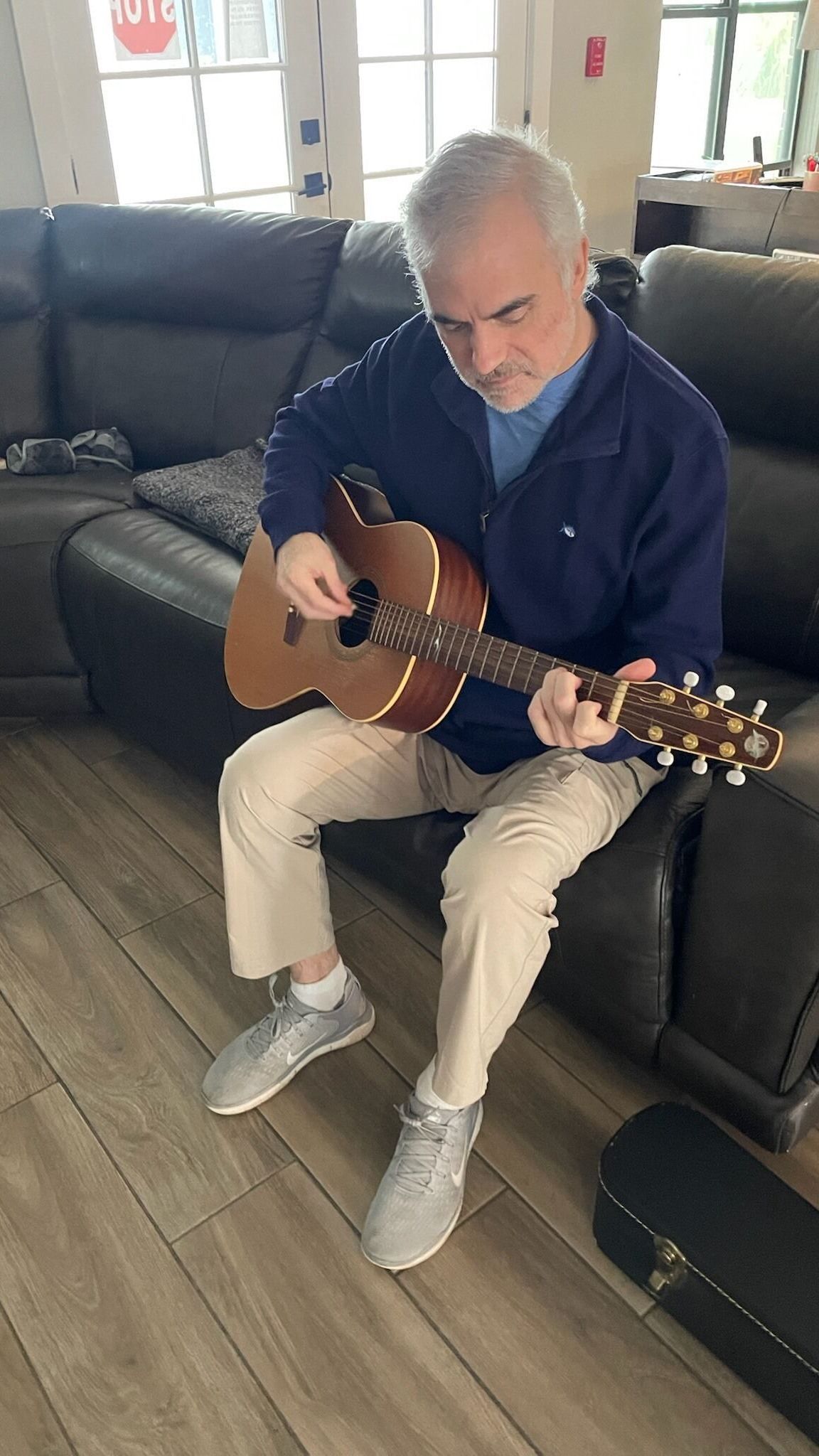 A man is sitting on a couch playing an acoustic guitar.