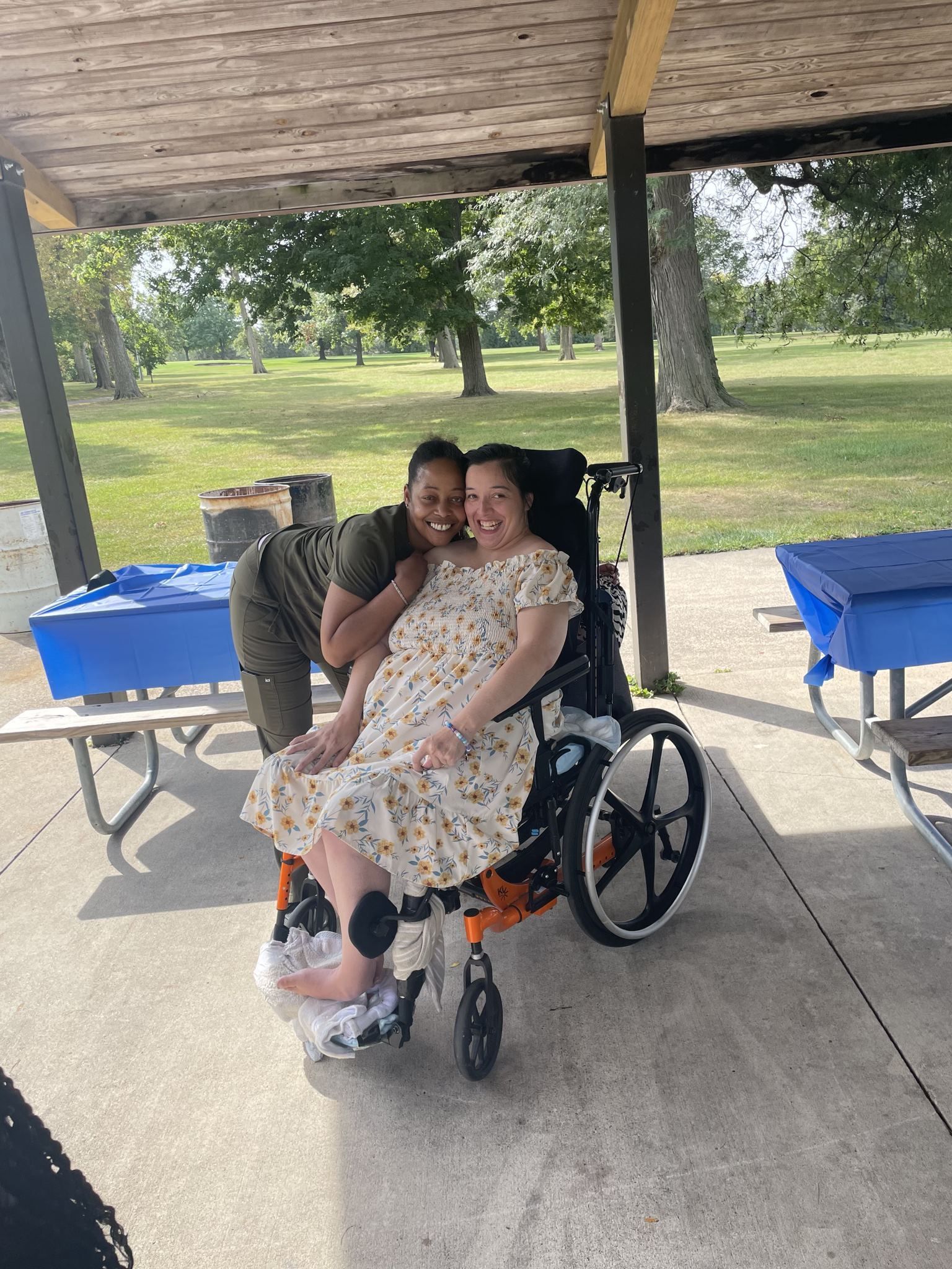 A woman in a wheelchair is hugging another woman in a park.