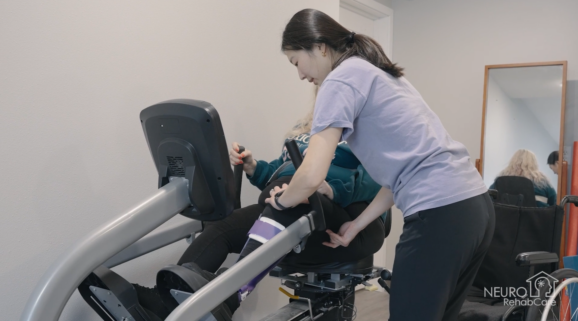 A woman is helping a man in a wheelchair on an exercise bike.