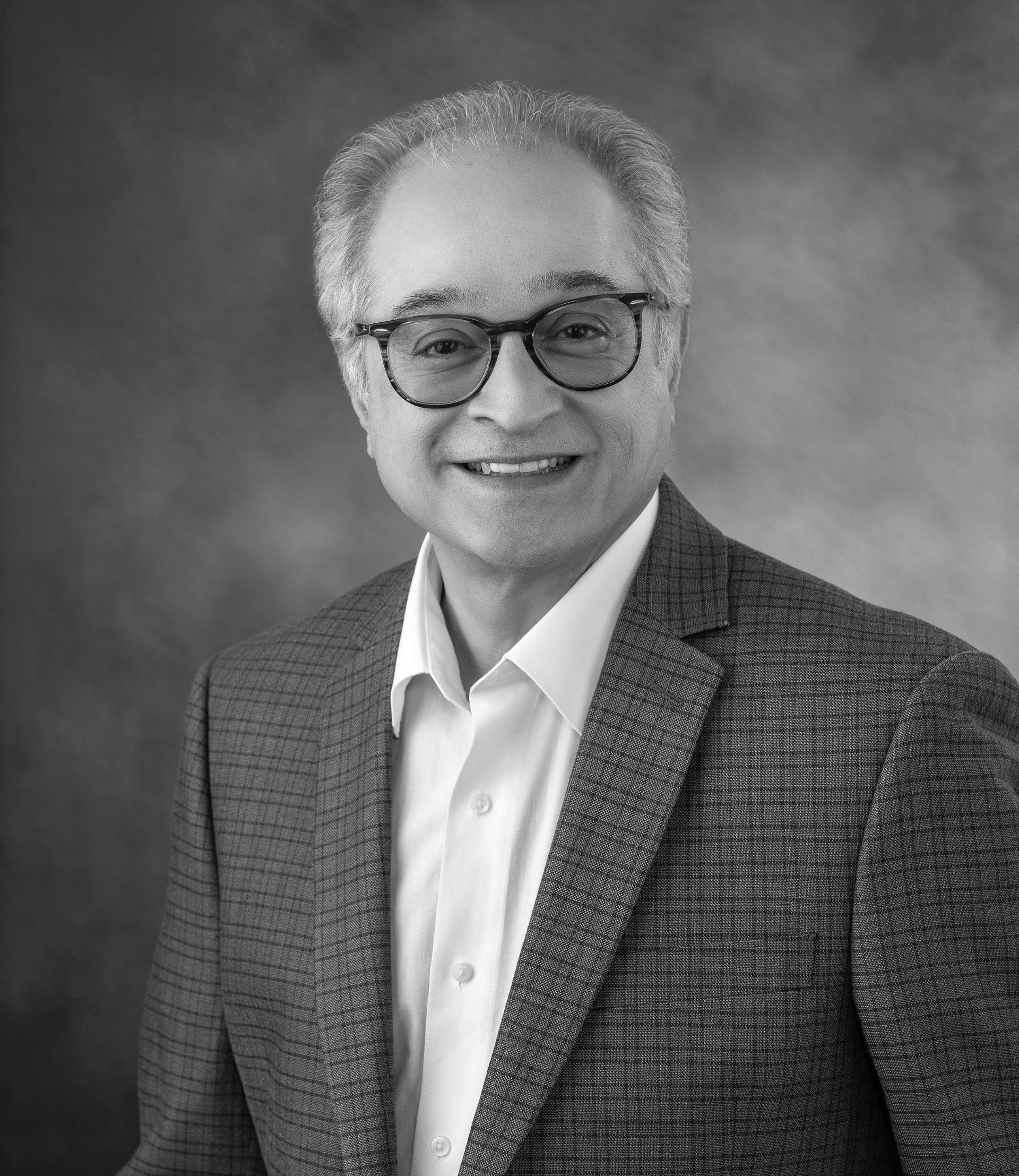 A man in a suit and glasses is smiling in a black and white photo.