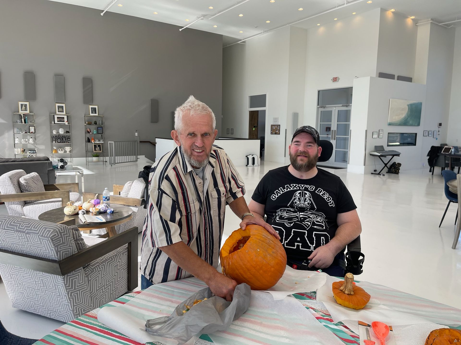 Two men are carving pumpkins in a living room.