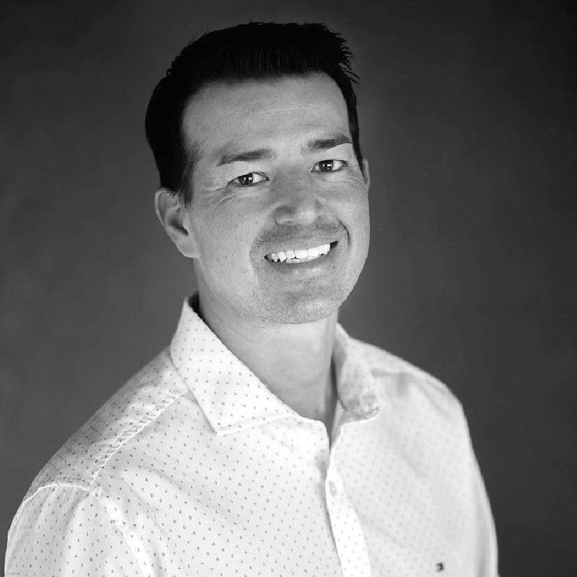 A man in a white shirt is smiling in a black and white photo.