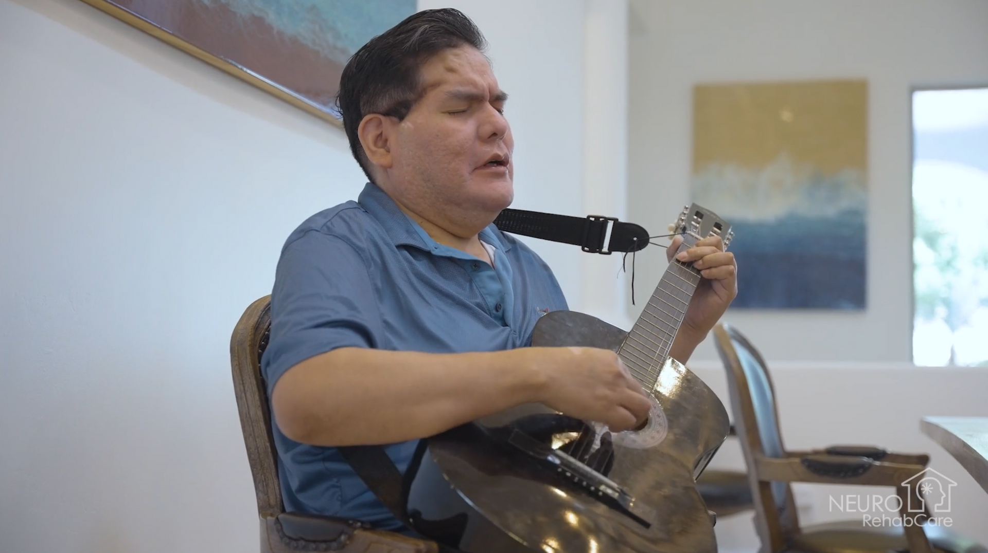 A man is sitting in a chair playing a guitar and singing into a microphone.