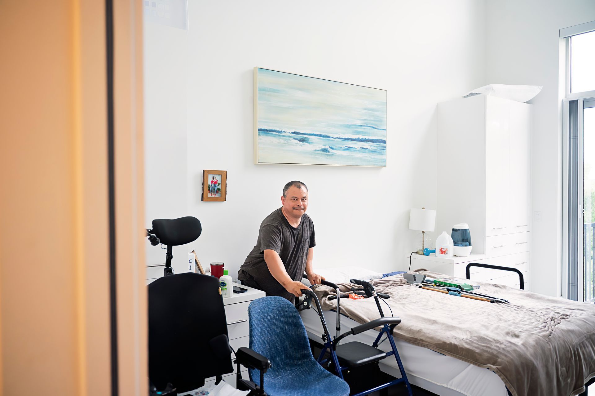A man in a wheelchair is standing next to a bed in a bedroom.