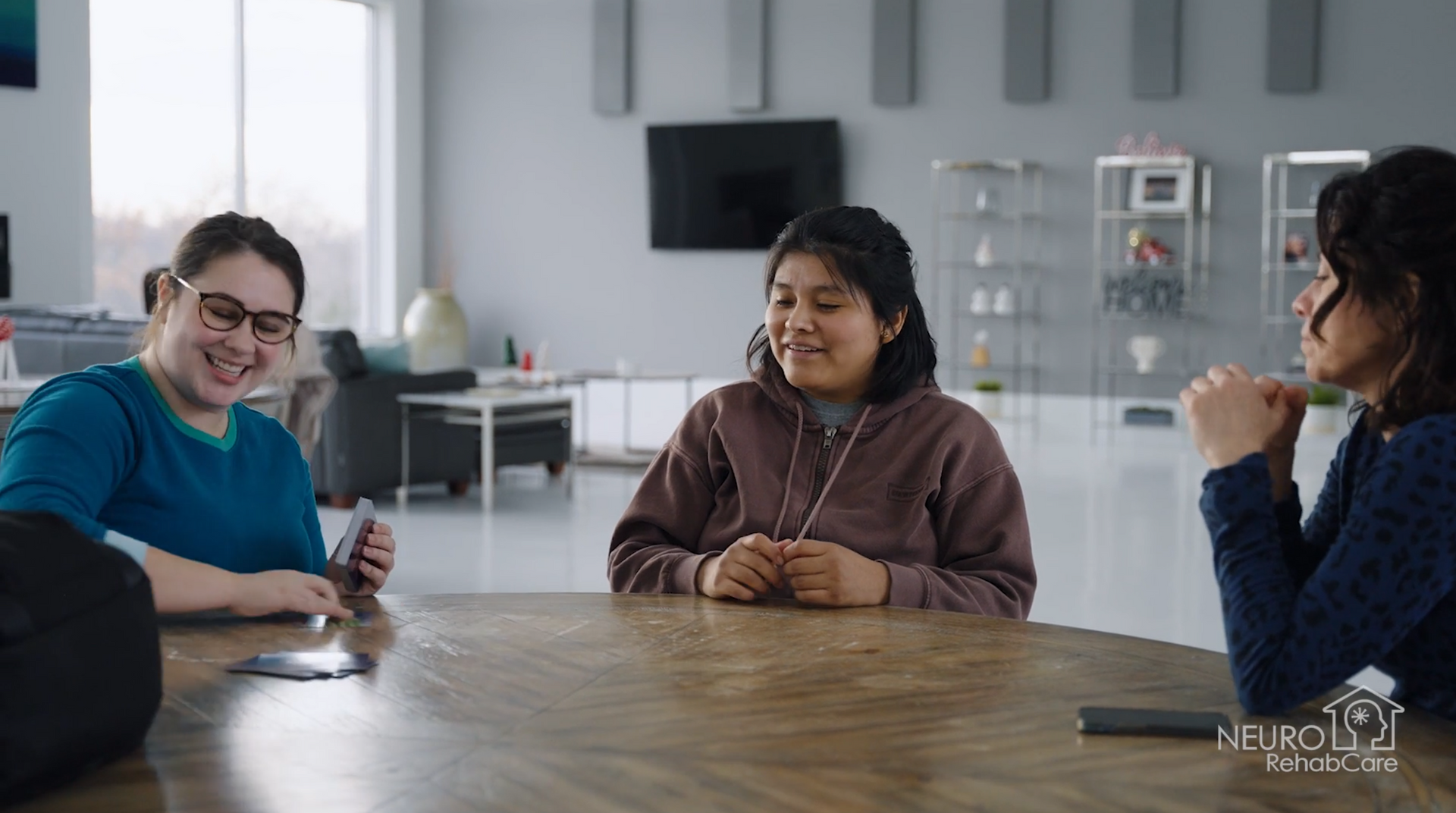 Three women are sitting at a table in a living room.