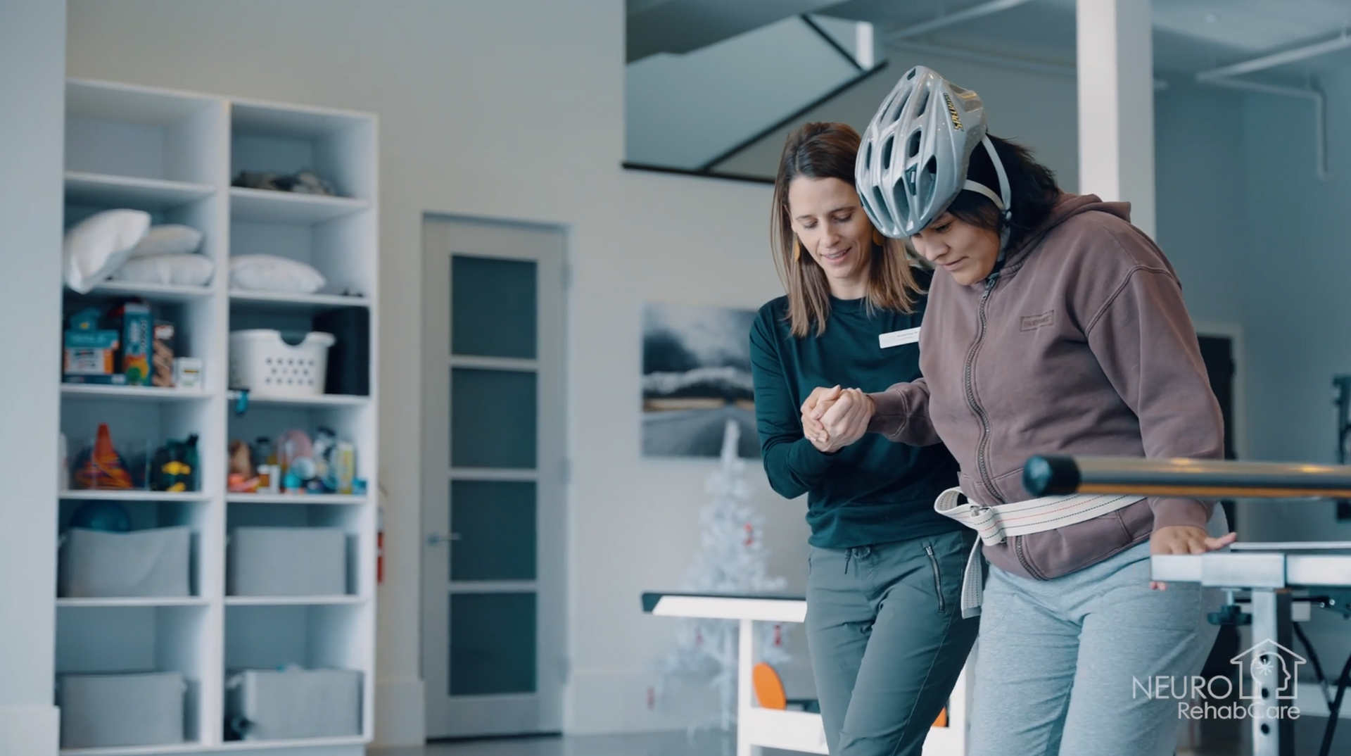 Two women are standing next to each other in a room . one of the women is wearing a helmet.