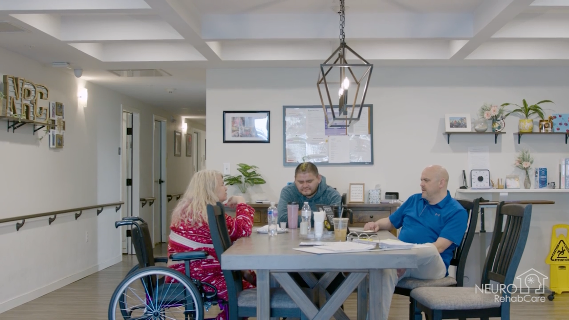 A group of people are sitting around a table with a christmas tree in the background.