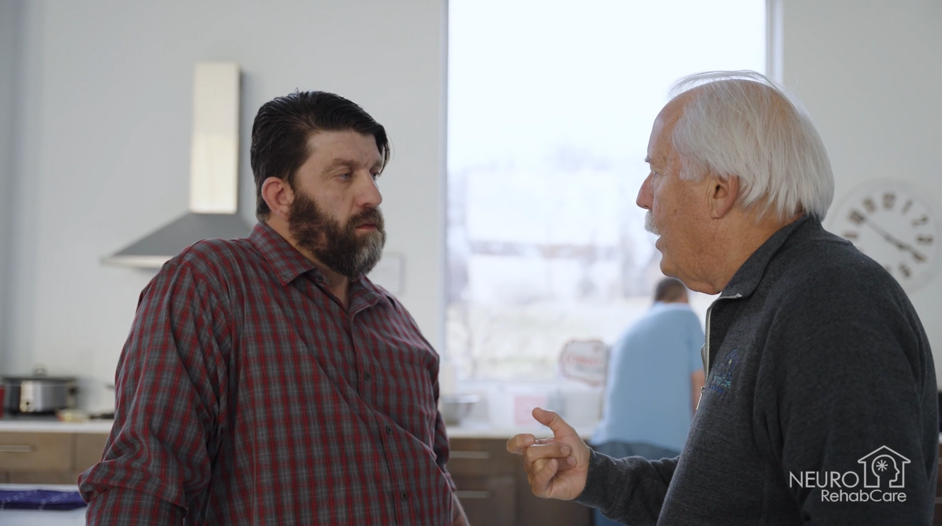 Two men are talking to each other in a kitchen.