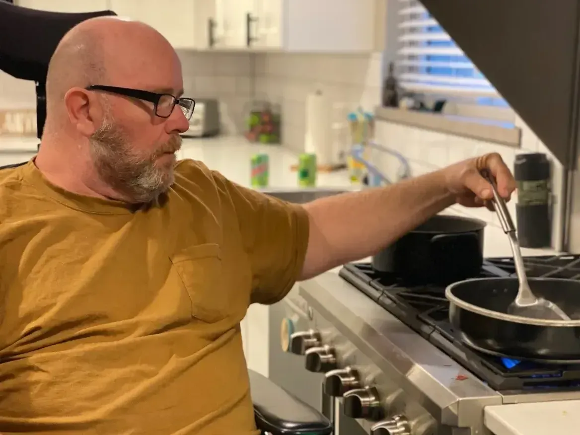 A man in a wheelchair is stirring a pot on a stove.