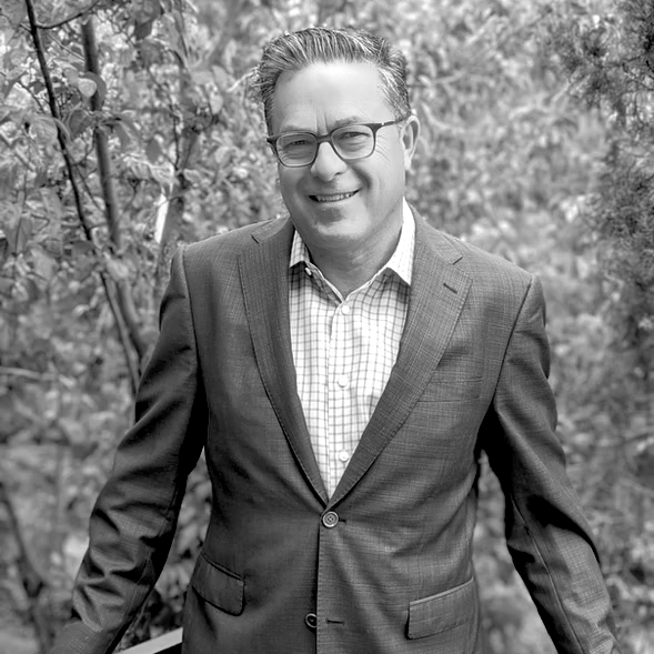 A man in a suit and glasses is smiling in a black and white photo.