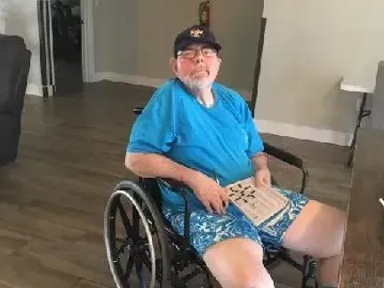 A man is sitting in a wheelchair in a living room holding a piece of paper.