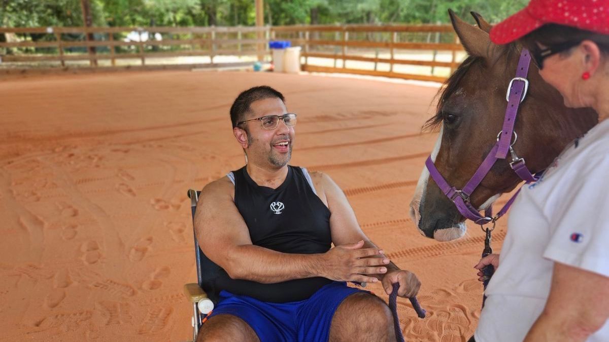A man in a wheelchair is talking to a woman riding a horse.