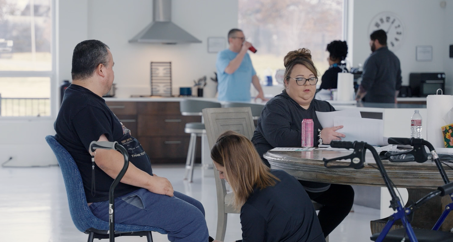 A group of people are sitting around a table in a kitchen.