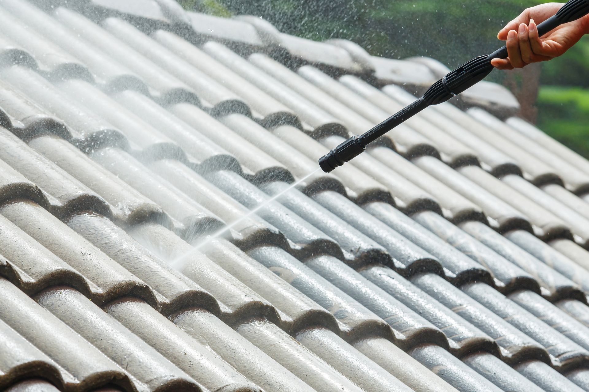 A person is cleaning a tiled roof with a high pressure washer.