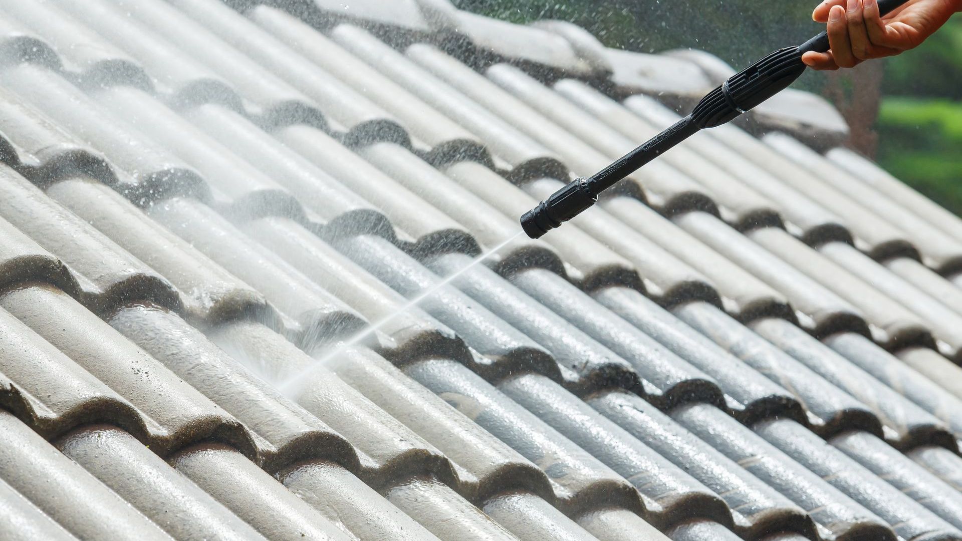A person is cleaning a roof with a high pressure washer.