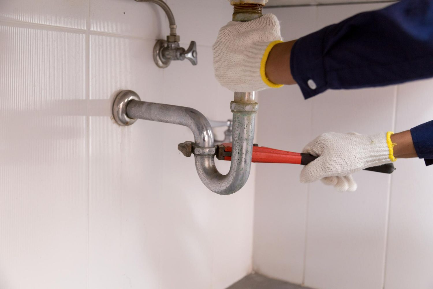 A plumber is fixing a sink pipe with a wrench.