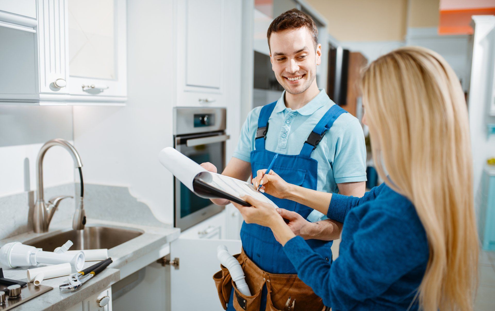 a man and a woman are standing in a kitchen looking at a clipboard .