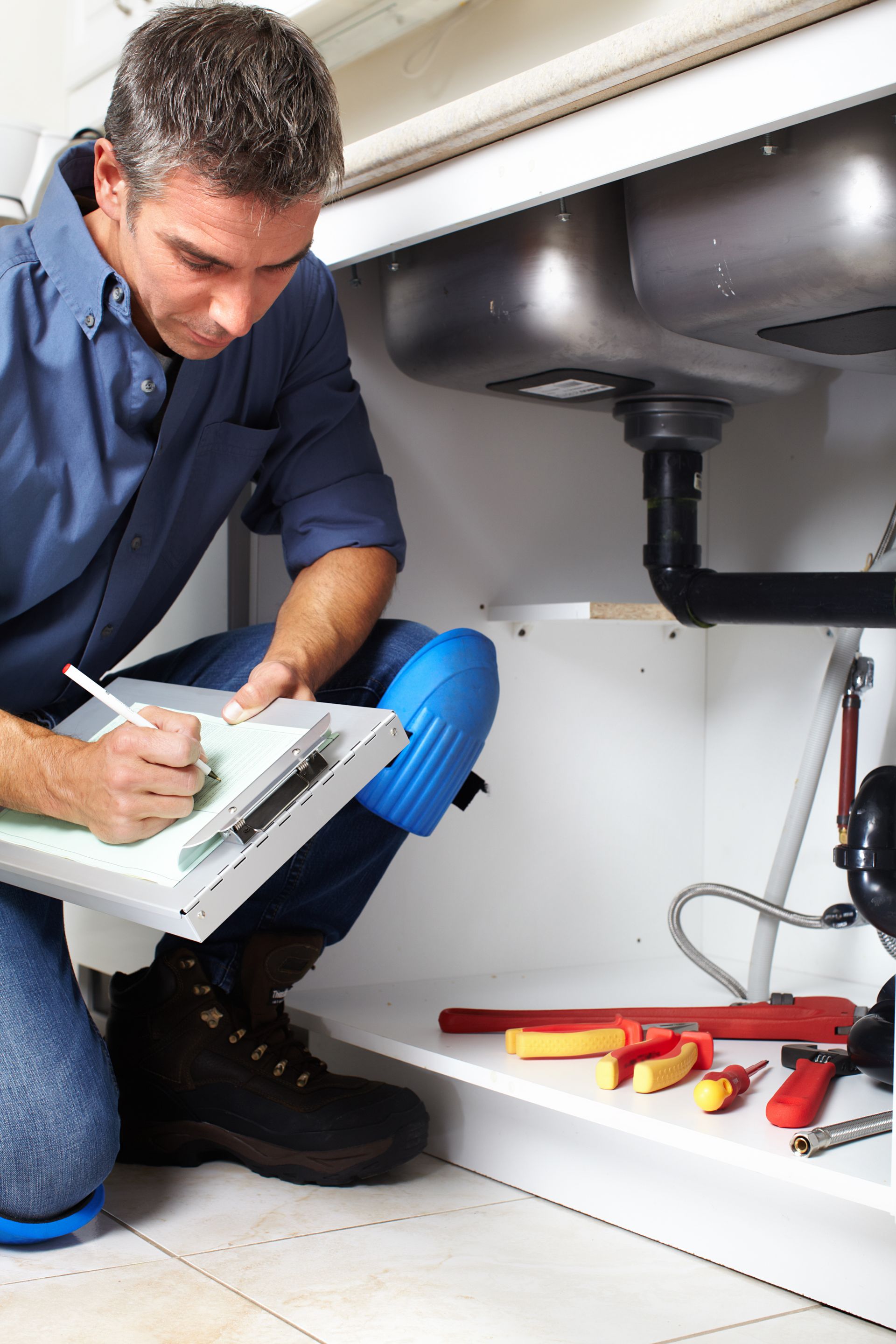 a plumber is kneeling under a sink and writing on a clipboard .