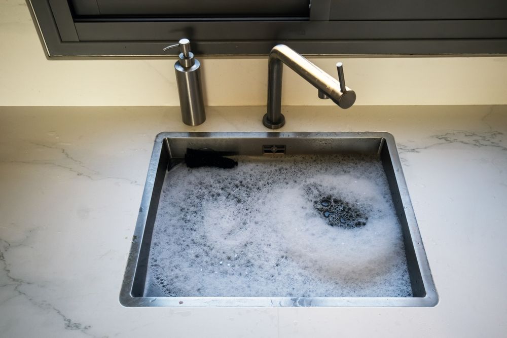 A kitchen sink filled with soapy water and a soap dispenser