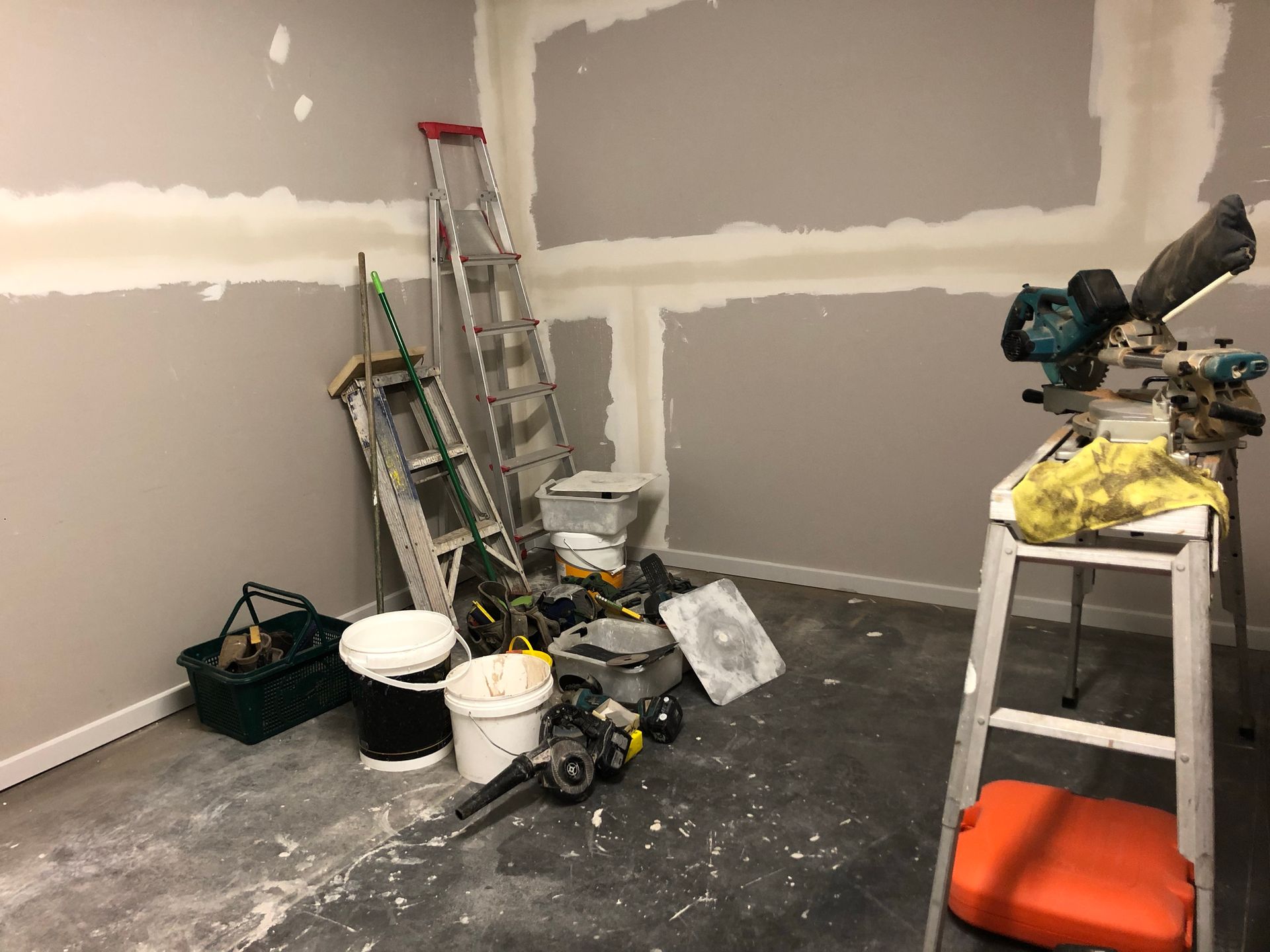 A room with a ladder , buckets , and tools on the floor.