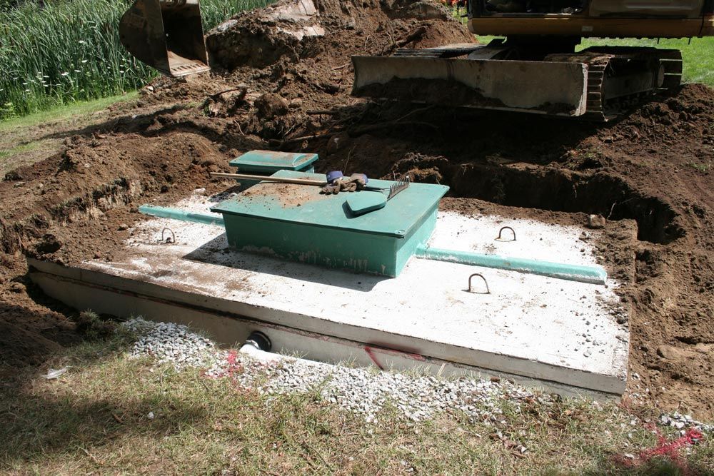 A septic tank is being built in the dirt with a bulldozer in the background.