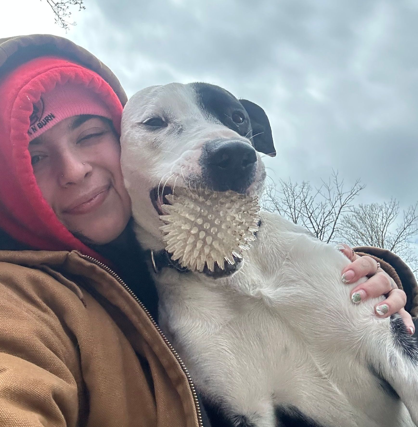A woman is holding a dog with a ball in its mouth.