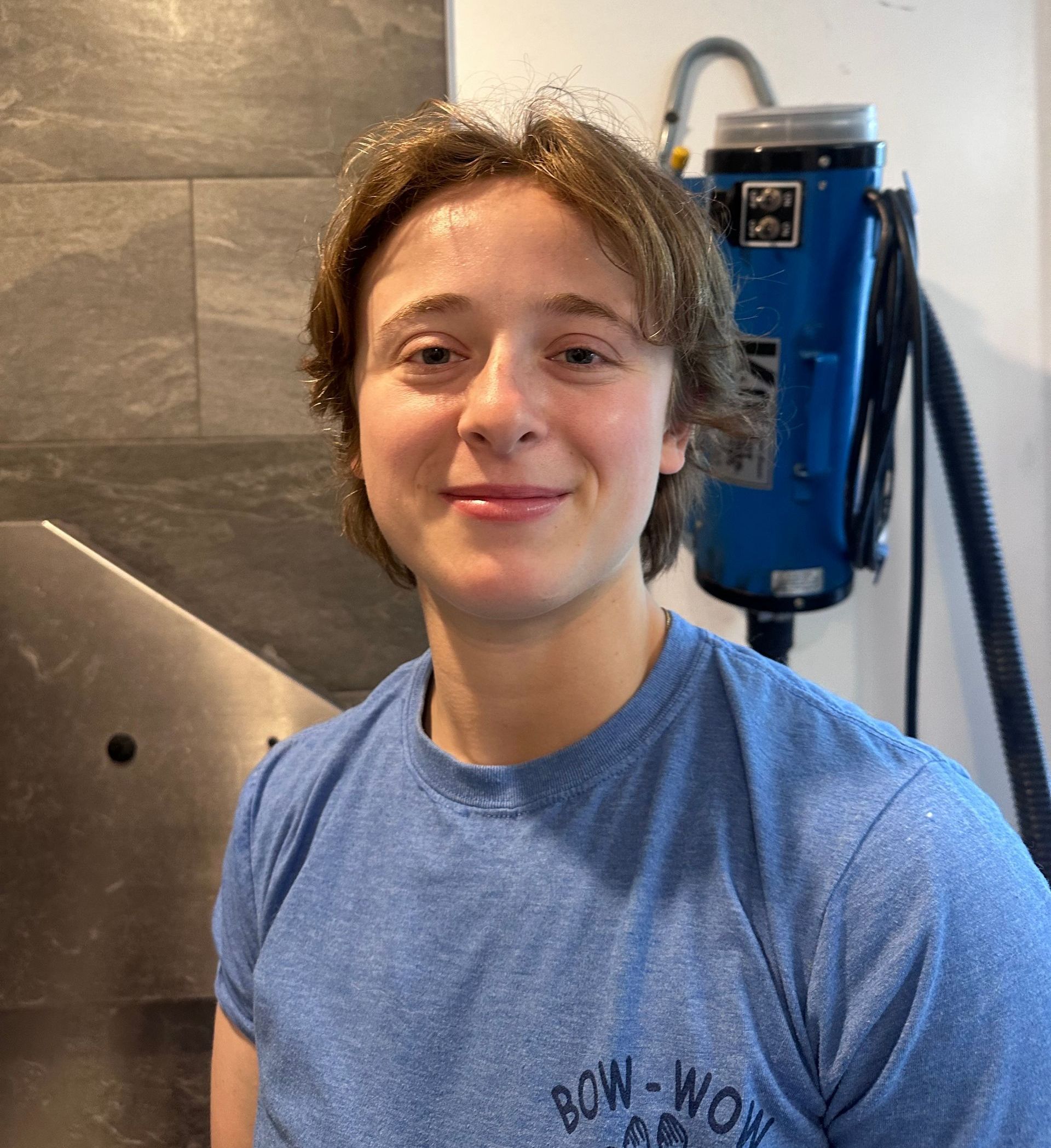 A young man in a blue shirt is standing in front of a vacuum cleaner.