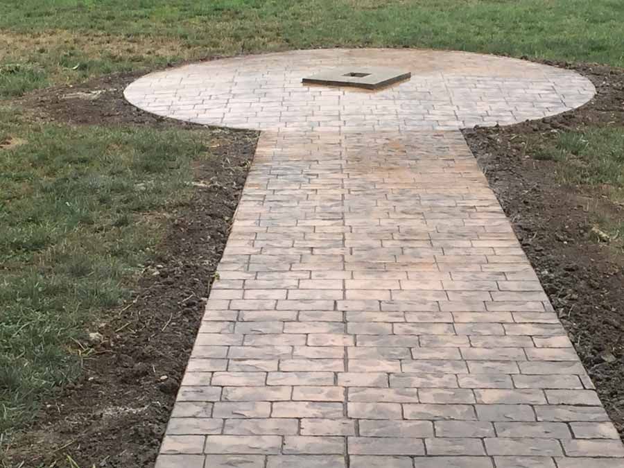 A brick walkway leading to a circle in the middle of a grassy field.