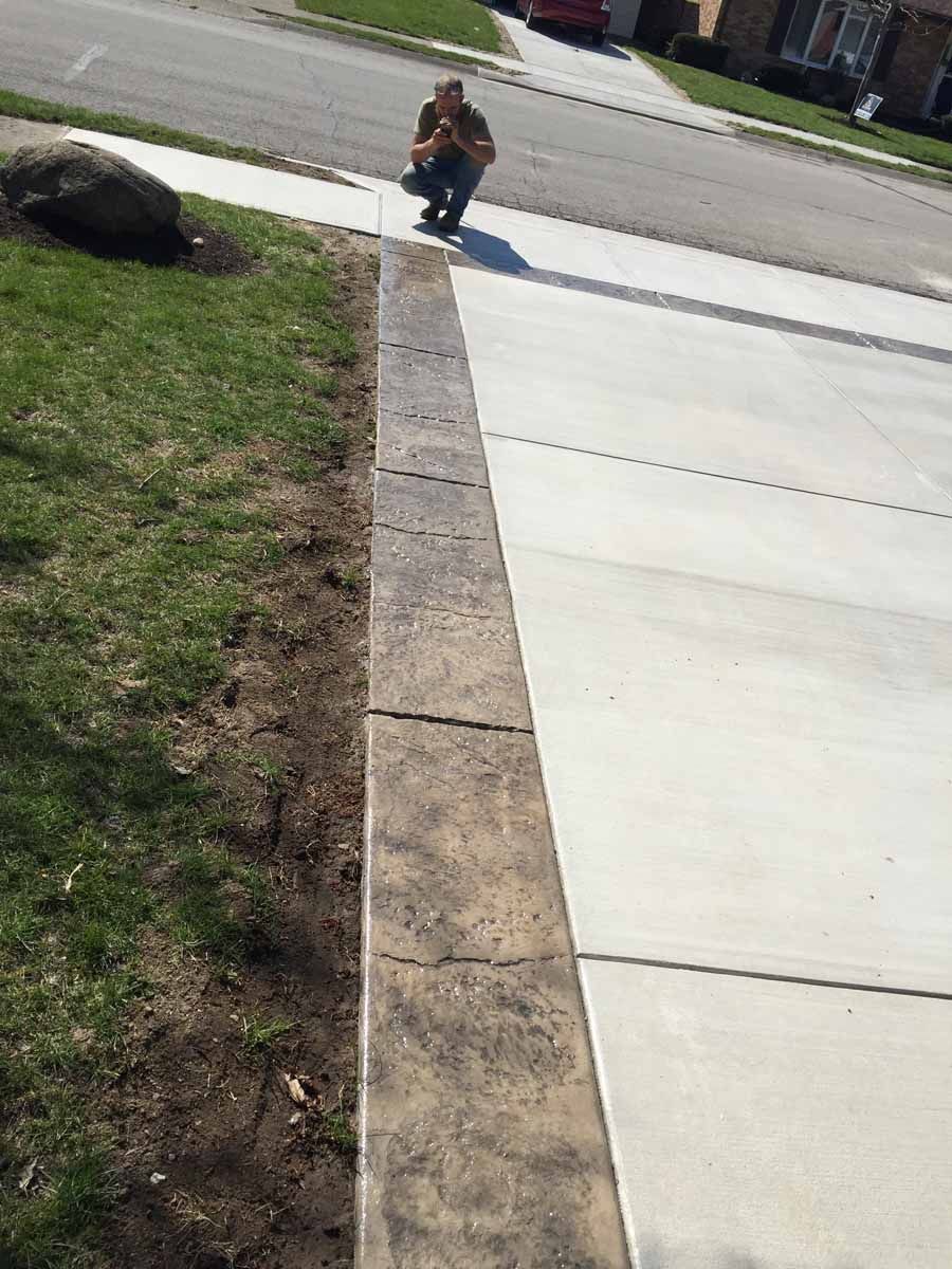 A man is kneeling down on a sidewalk next to a concrete curb.
