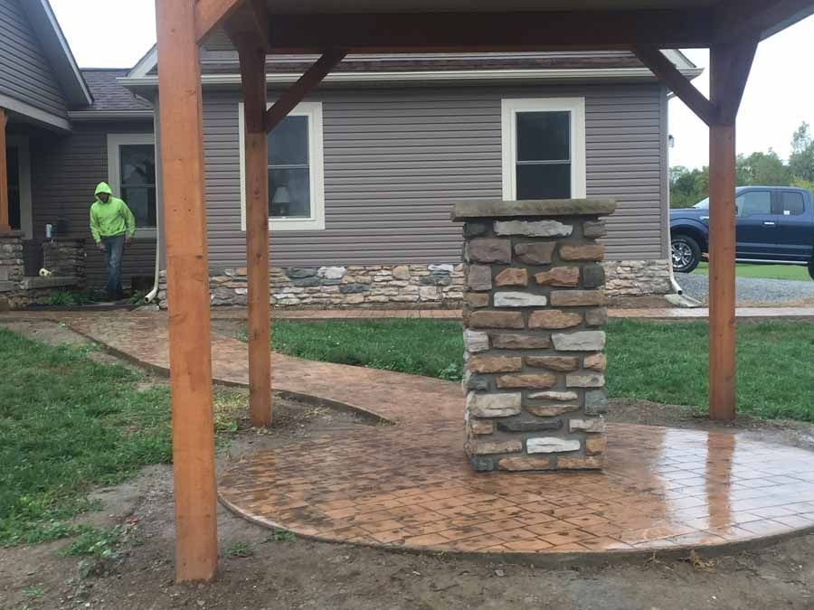 A brick pillar is sitting under a wooden structure in front of a house.