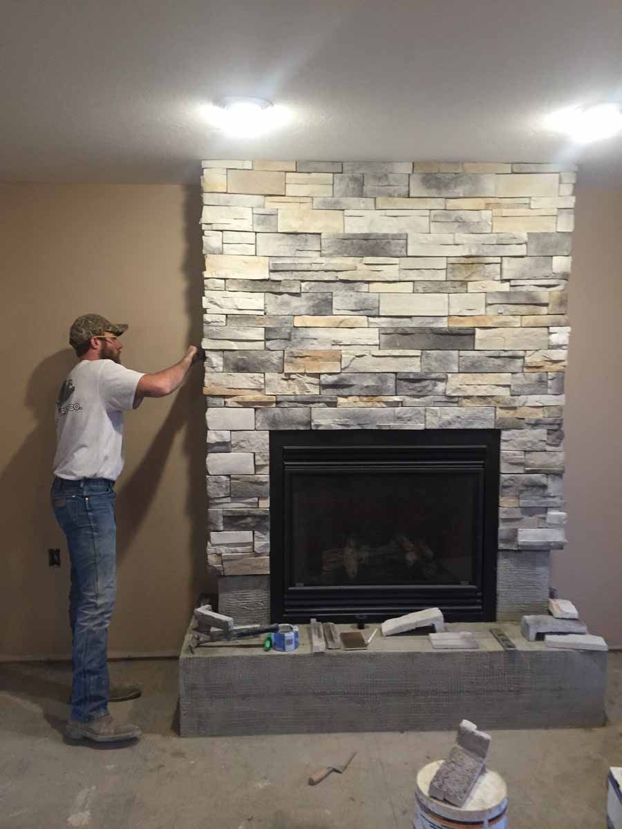 A man is working on a stone fireplace in a living room.