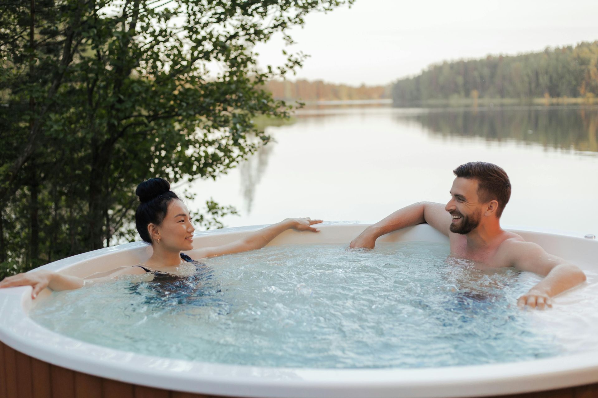 A man and a woman are sitting in a hot tub next to a lake.
