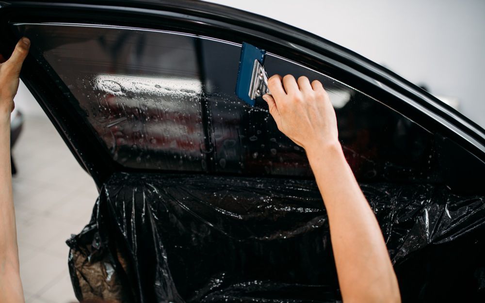Person applying tint film to a car window with a squeegee.