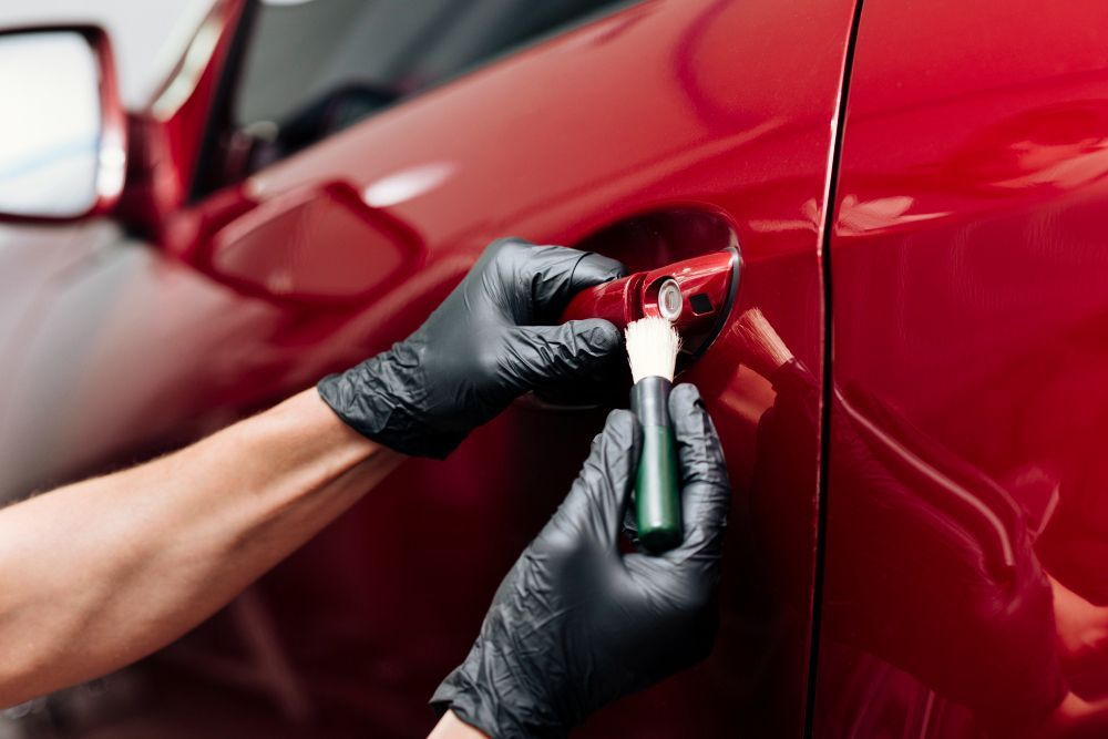 Gloved hands applying ceramic coating to a red car door handle.