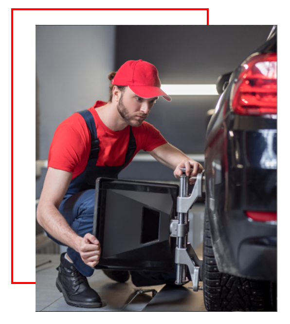 Mechanic aligning car wheel in a garage, wearing red cap and overalls.