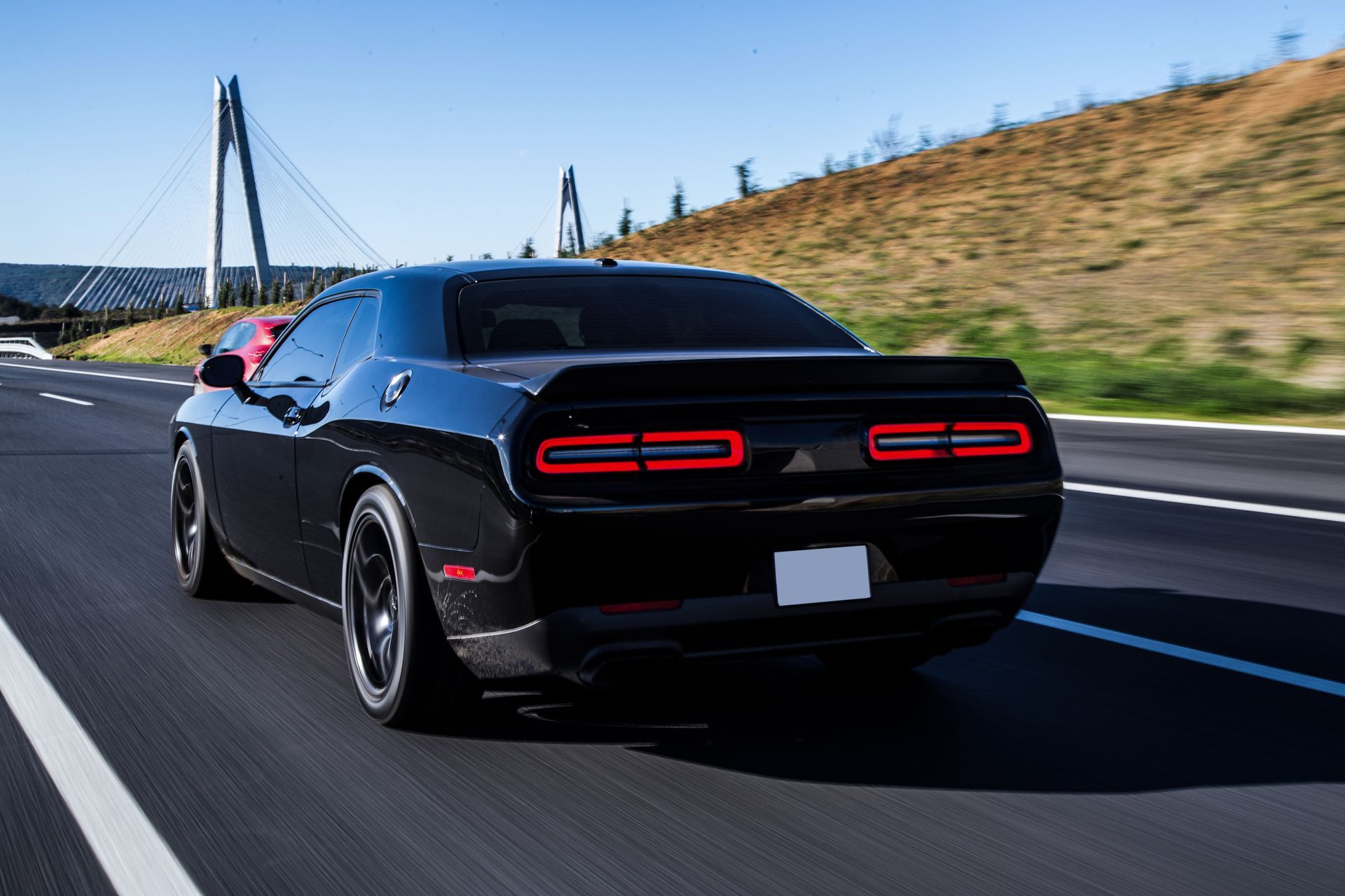 Black Dodge Challenger driving on a highway, with a bridge in the background.