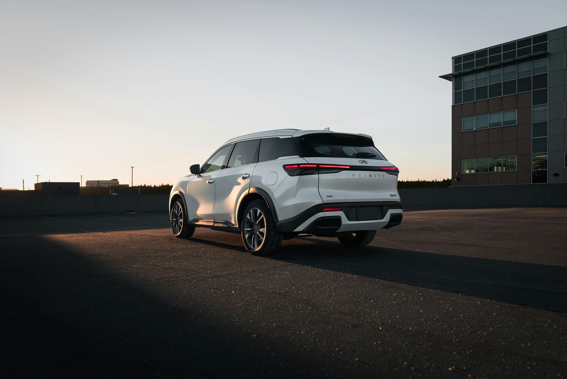 White SUV parked on asphalt, near a building at sunset.