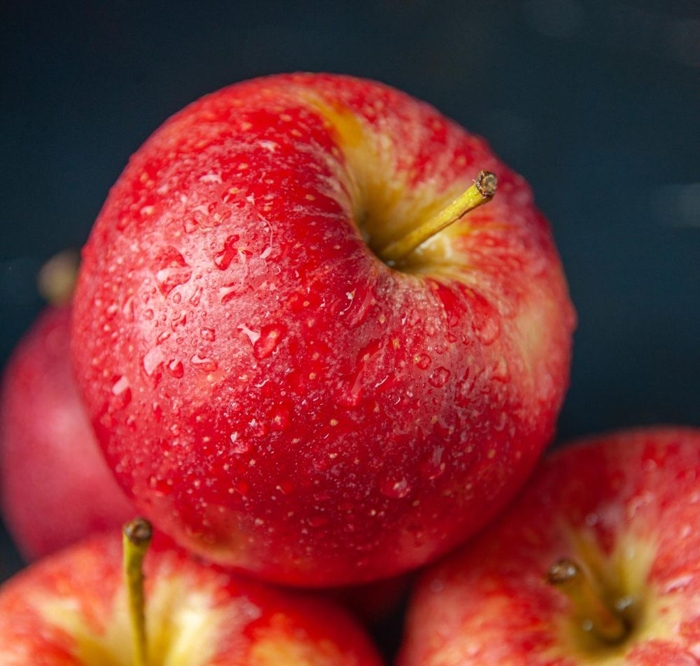 Manzanas rojas, primer plano con gotas de agua, apiladas, fondo oscuro.