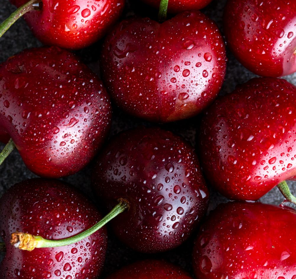 Primer plano de cerezas rojas maduras con gotas de agua, sobre una superficie oscura.