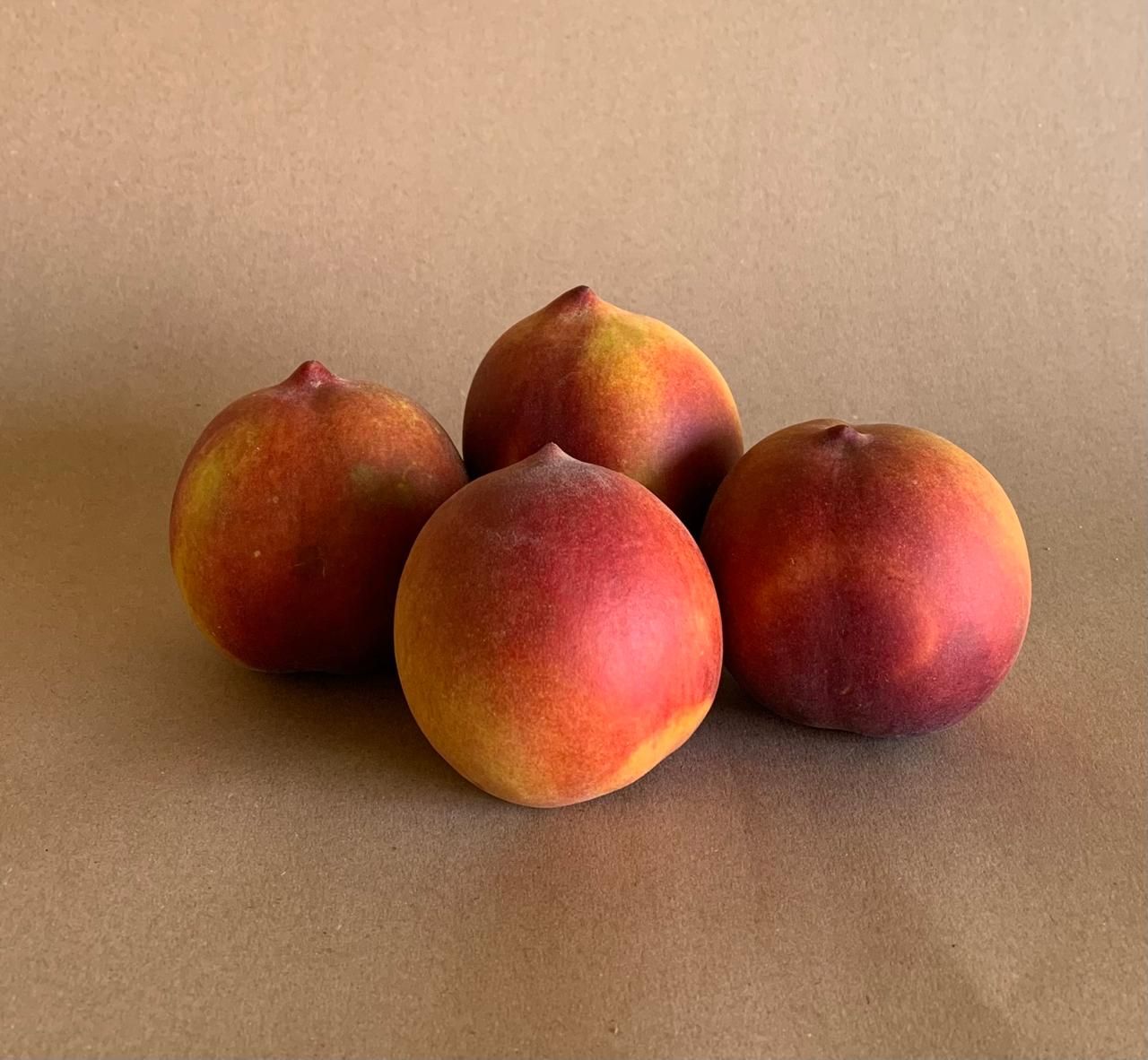 Cuatro melocotones maduros sobre una superficie de color canela; piel roja y amarilla.