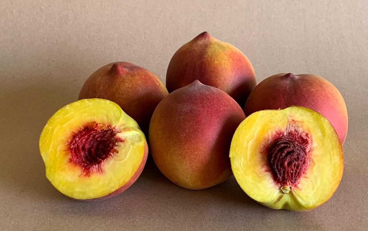 Melocotones con piel aterciopelada, uno de ellos cortado para mostrar el hueso rojo y la pulpa amarilla.